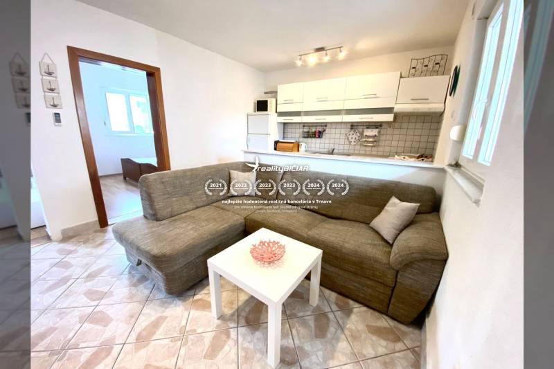 NIN-GRBLJANSKE VIKENDICE - dom s dvoma bytmi - Interiér rodinného domu s pohovkou, bielym stolom a kuchynským kútom.