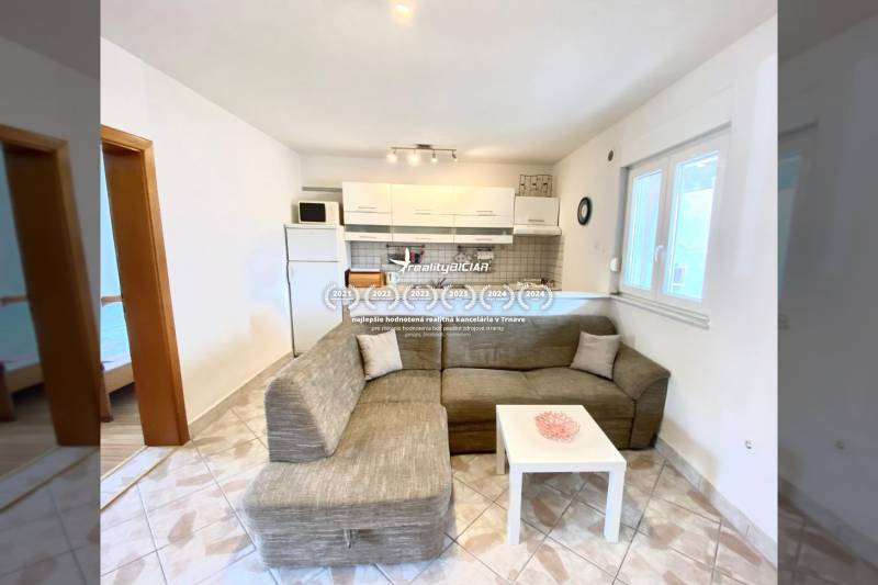 NIN-GRBLJANSKE VIKENDICE - dom s dvoma bytmi - Obývacia izba v rodinnom dome s pohovkou a kuchynským kútom, dlažba na podlahe.