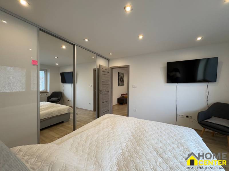 NA PREDAJ vkusne zrekonštruovaný  2 izbový byt, Komárno - Spálňa v 2-izbovom byte s televízorom, veľkou skriňou a podlahou s dreveným dekorom.