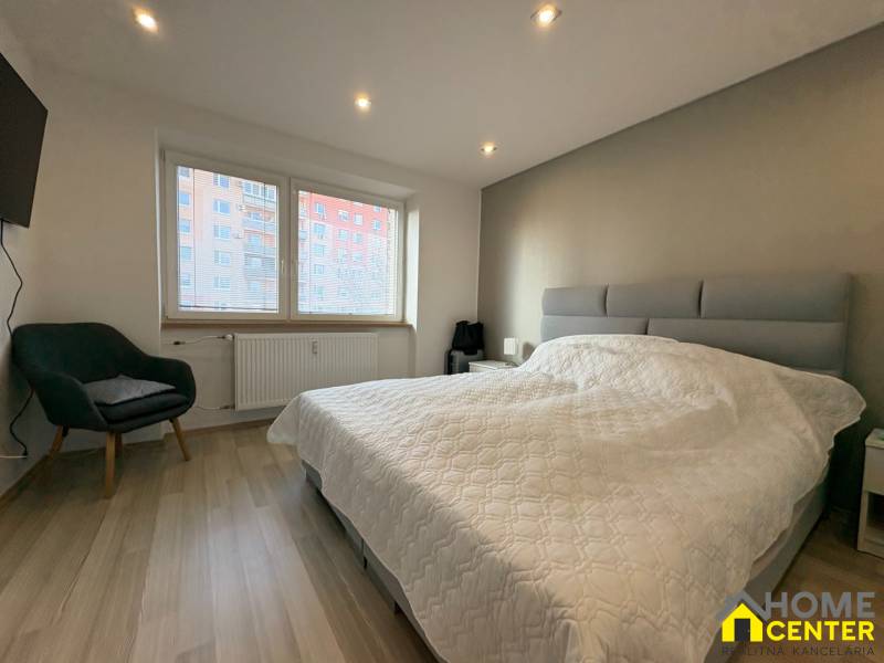 NA PREDAJ vkusne zrekonštruovaný  2 izbový byt, Komárno - Spálňa v 2-izbovom byte s podlahou s dreveným dekorom, pohodlným kreslom a veľkým oknom.