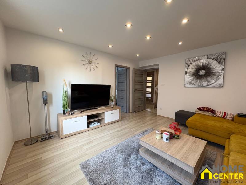 NA PREDAJ vkusne zrekonštruovaný  2 izbový byt, Komárno - Obývačka v 2-izbovom byte s podlahou s dreveným dekorom, TV a žltou pohovkou.