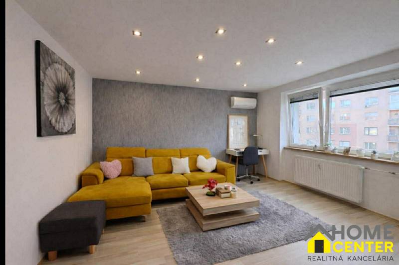 NA PREDAJ vkusne zrekonštruovaný  2 izbový byt, Komárno - Obývacia izba v 2-izbovom byte s pohovkou, podlaha s dreveným dekorom, šedý koberec.