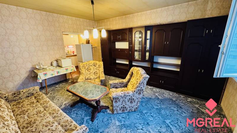 Na predaj 2 i byt v Partizánskom - Šípok - Obývacia izba v 2-izbovom byte so starším nábytkom a kobercom na podlahe.