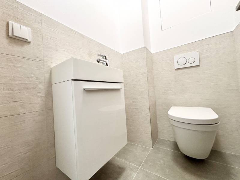 I PRENÁJOM - Nový moderný 2-izb. byt, TEHELNÉ POLE, Bajkalská - Skrytá toaleta v 2-izbovom byte na ulici Bajkalská, minimalistické biele umývadlo a vešiak.