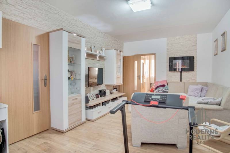 3-izbový byt s loggiou na ul. S.H. Vajanského, Nové Zámky – 74,69m2 - Obývacia izba v 3-izbovom byte s podlahou s dreveným dekorom a rohovou sedačkou.