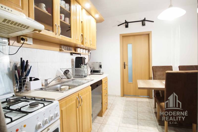 3-izbový byt s loggiou na ul. S.H. Vajanského, Nové Zámky – 74,69m2 - Kuchyňa v 3-izbovom byte s drevenými skrinkami a jedálenským stolom.