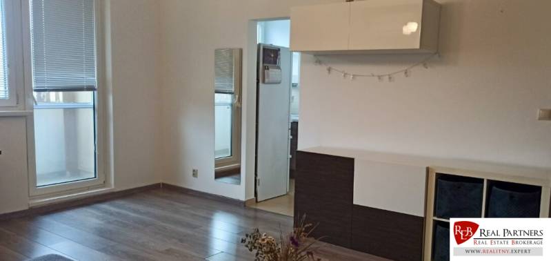 Prenájom 2-izbový byt na začiatku Petržalky - Obývacia izba v 2-izbovom byte s podlahou s dreveným dekorom, bielym nábytkom a zrkadlom.