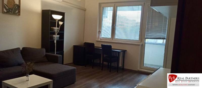 Prenájom 2-izbový byt na začiatku Petržalky - Obývacia izba v 2-izbovom byte s rohovou sedačkou a podlahou s dreveným dekorom.