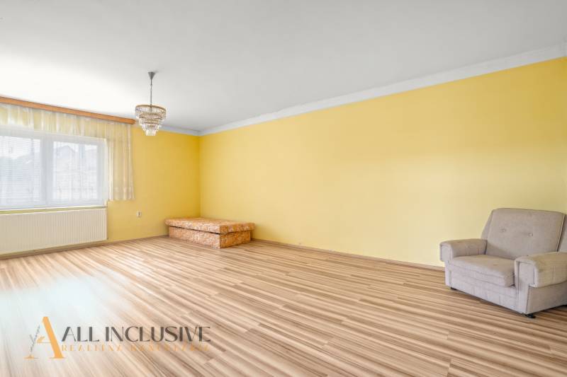 NA PREDAJ 3-IZBOVÝ RODINNÝ DOM, PUSTÉ ÚĽANY - Žltá izba s kreslom a pohovkou, podlaha s dreveným dekorom.