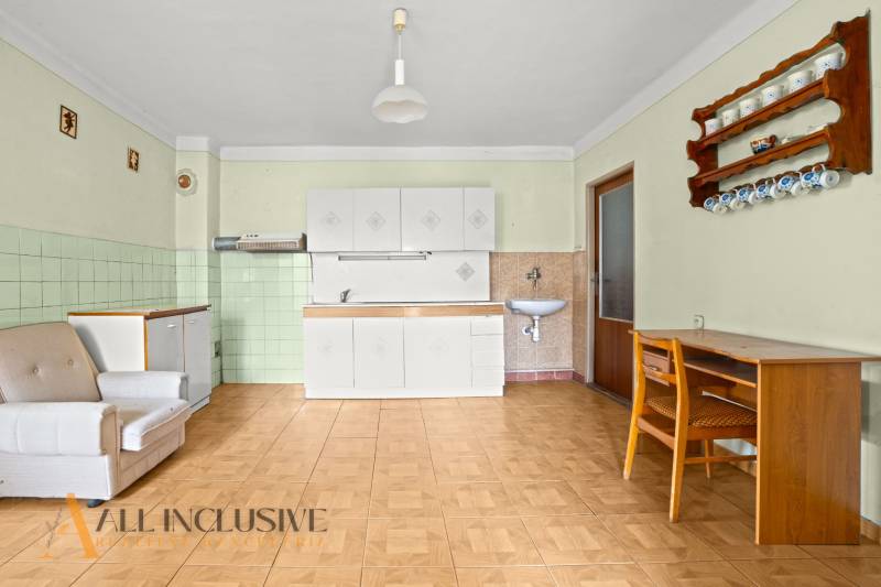 NA PREDAJ 3-IZBOVÝ RODINNÝ DOM, PUSTÉ ÚĽANY - Interiér rodinného domu s kuchynskou linkou, kreslom a stolom, podlaha s dreveným dekorom.