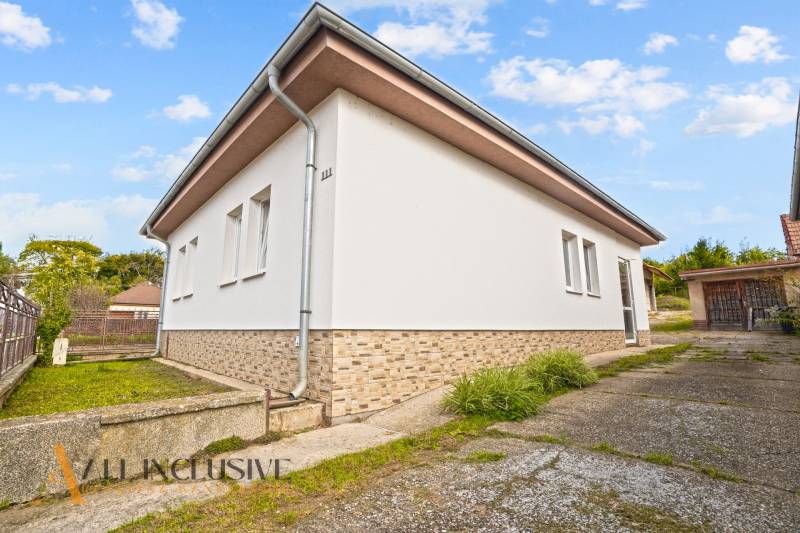 NA PREDAJ 5-IZBOVÝ RODINNÝ DOM NA 15Á POZEMKU,ŠALGOČKA - Rodinný dom v Šalgočke s bielou fasádou, okolitou zeleňou a betónovou prístupovou cestou.