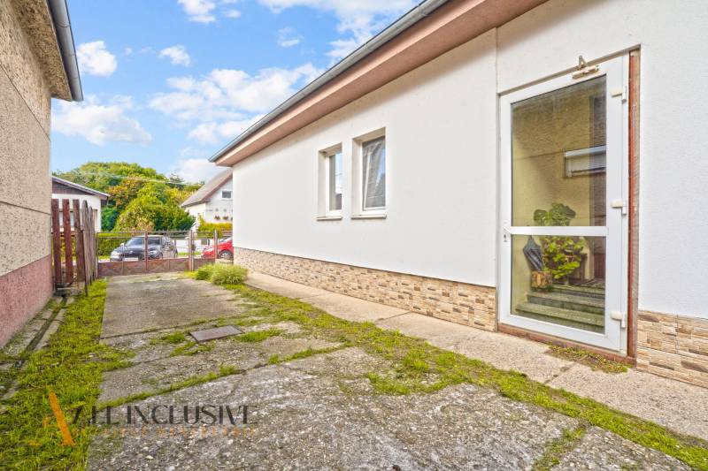 NA PREDAJ 5-IZBOVÝ RODINNÝ DOM NA 15Á POZEMKU,ŠALGOČKA - Rodinný dom v Šalgočke s betónovým chodníkom, bielou fasádou a sklenými dverami.