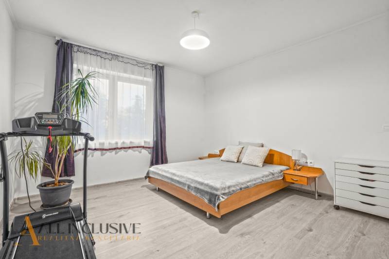 REZERVOVANÉ 5-IZBOVÝ RODINNÝ DOM VO VEĽKEJ PAKE - Svetlá spálňa s posteľou, bežeckým pásom, rastlinou a podlahou s dreveným dekorom v rodinnom dome.