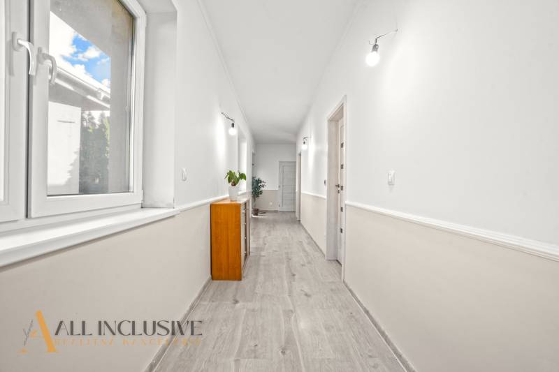 REZERVOVANÉ 5-IZBOVÝ RODINNÝ DOM VO VEĽKEJ PAKE - Chodba s podlahou s dreveným dekorom v rodinnom dome, biele steny, nábytok a rastliny.