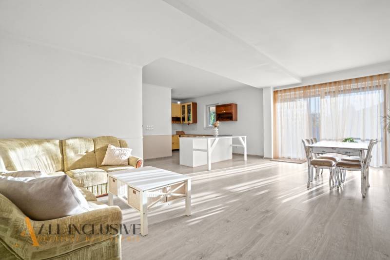 REZERVOVANÉ 5-IZBOVÝ RODINNÝ DOM VO VEĽKEJ PAKE - Obývacia izba s kuchyňou a podlahou s dreveným dekorom v rodinnom dome.