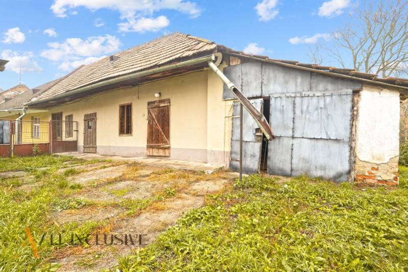 NA PREDAJ 4-IZBOVÝ RODINNÝ DOM V OBCI MOSTOVÁ - Rodinný dom v Mostovej s plechovou prístavbou, okolitým trávnikom a drevenými dverami.