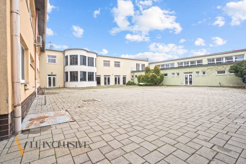 NA PREDAJ ŠKOLSKÁ BUDOVA NA VEĽKOM POZEMKU, MOSTOVÁ - Budova v Mostovej s dláždeným nádvorím a presklenými balkónmi, obloha s oblakmi.