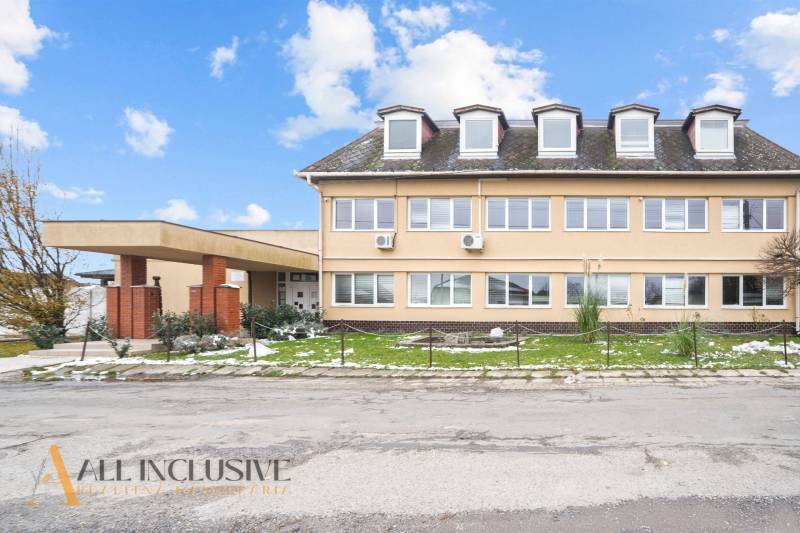 NA PREDAJ ŠKOLSKÁ BUDOVA NA VEĽKOM POZEMKU, MOSTOVÁ - Budova v Mostovej s oknami v podkroví, tehlovými stĺpmi a trávnikom so snehom.