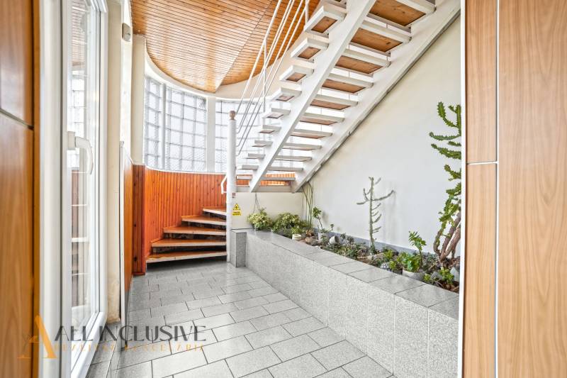 NA PREDAJ ŠKOLSKÁ BUDOVA NA VEĽKOM POZEMKU, MOSTOVÁ - Interiér budovy s bielymi schodmi, podlaha s dreveným dekorom, zeleň.