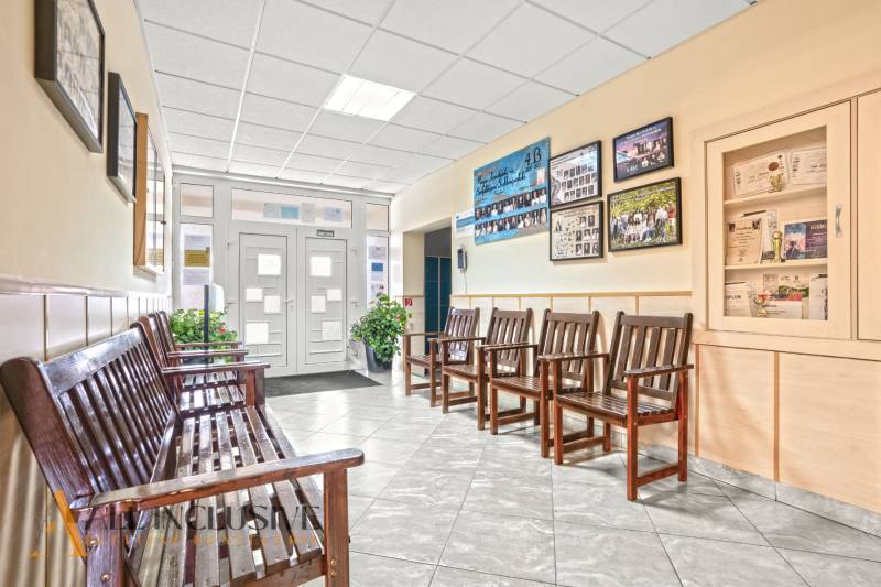 NA PREDAJ ŠKOLSKÁ BUDOVA NA VEĽKOM POZEMKU, MOSTOVÁ - Budova s lavičkami a vitrínami na stene, dlaždicová podlaha, dekorácie a rastliny.