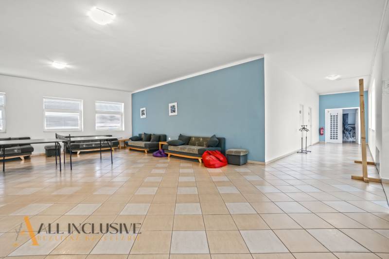 NA PREDAJ ŠKOLSKÁ BUDOVA NA VEĽKOM POZEMKU, MOSTOVÁ - Interiér budovy s podlahou s dreveným dekorom, sedacími súpravami a modrou stenou.