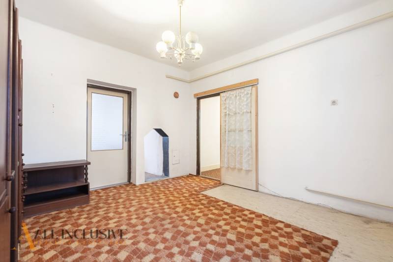 Na predaj 4-izbový rodinný dom, Gabčíkovo - Izba v rodinnom dome s lustrom, štruktúrovanou podlahou a dreveným nábytkom.