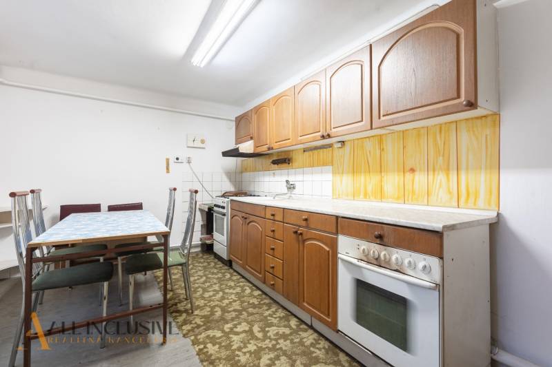 Na predaj 4-izbový rodinný dom, Gabčíkovo - Kuchyňa v rodinnom dome s drevenými skrinkami a kobercom pri jedálenskom stole.