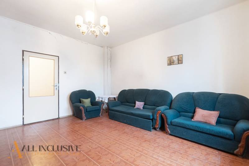 Na predaj 4-izbový rodinný dom, Gabčíkovo - Obývacia izba s tmavozelenou sedačkou, podlahou s dreveným dekorom a svetlom na strope.