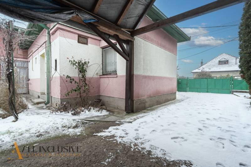 Na predaj 4-izbový rodinný dom, Gabčíkovo - Zasnežený dvor rodinného domu v Gabčíkove s ružovo-bielou fasádou a zelenou bránou.