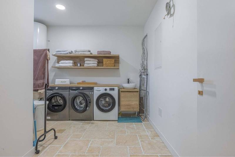 NA PREDAJ 4 IZB RD S DVOJGARÁŽOU, DUNAJSKÁ STREDA - Práčovňa v rodinnom dome s práčkami, poličkou, uterákmi a podlahou s kamenným dekorom.