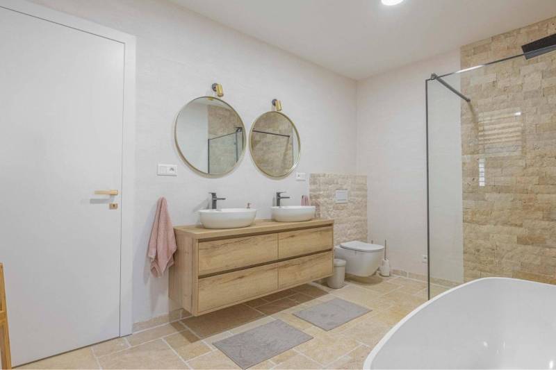 NA PREDAJ 4 IZB RD S DVOJGARÁŽOU, DUNAJSKÁ STREDA - Kúpeľňa s dvoma okrúhlymi zrkadlami a kamenným obkladom v rodinnom dome.