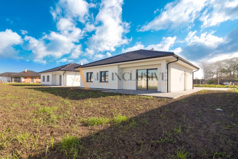 NA PREDAJ 4 IZBOVÝ RODINNÝ DOM-NOVOSTAVBA, KRÁĽOV BROD - Rodinný dom s bielou fasádou a tmavou strechou uprostred zelenej lúky.