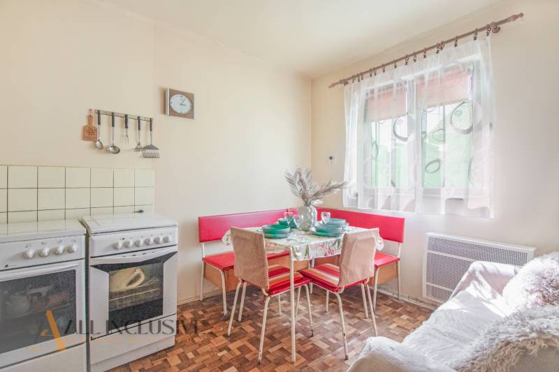 NA PREDAJ 4-IZBOVÝ RODINNÝ DOM NA PRIESTRANNOM POZEMKU - Kuchyňa v rodinnom dome s retro nábytkom, stôl, stoličky, varič, okno so závesmi.