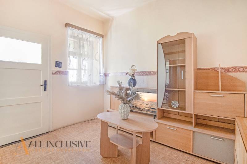 NA PREDAJ 4-IZBOVÝ RODINNÝ DOM NA PRIESTRANNOM POZEMKU - Obývacia izba rodinného domu s dreveným nábytkom a dekoratívnou vázou na stole.