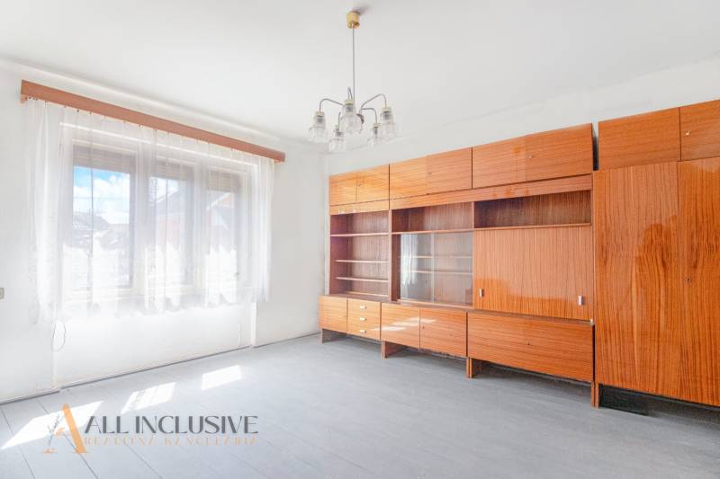 NA PREDAJ RODINNÝ DOM NA 9,5 ÁROVOM POZEMKU, OHRADY - Izba v rodinnom dome, drevená zostava nábytku, biele steny a závesy.