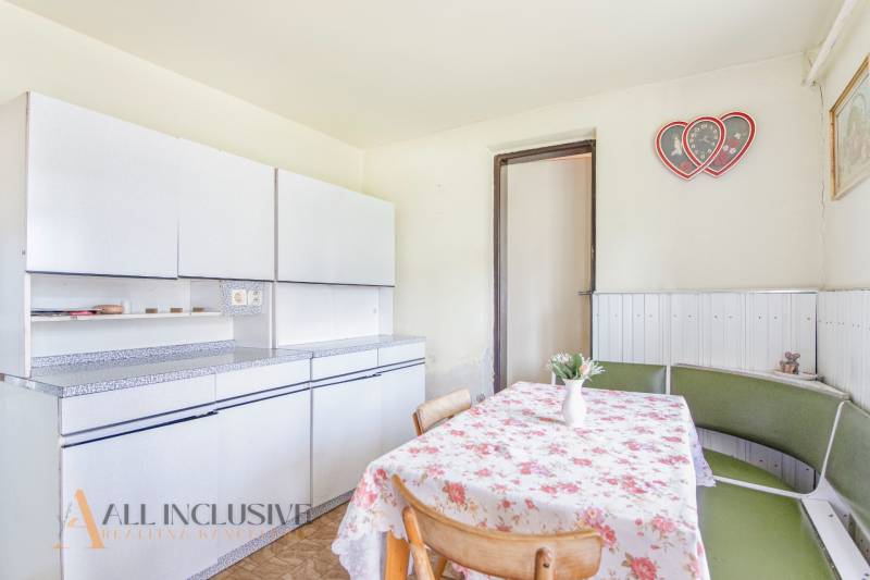 NA PREDAJ RODINNÝ DOM NA 9,5 ÁROVOM POZEMKU, OHRADY - Kuchyňa rodinného domu s bielymi skrinkami, kvetinovým obrusom a dekoráciou v tvare srdca.