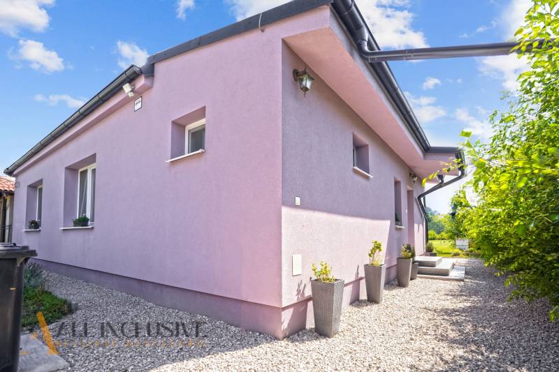 REZERVOVANÉ 3-IZBOVÝ RODINNÝ DOM V OBCI BALOŇ - Rodinný dom v Baloňi v svetlofialovej fasáde so štrkovým chodníkom a kvetináčmi.