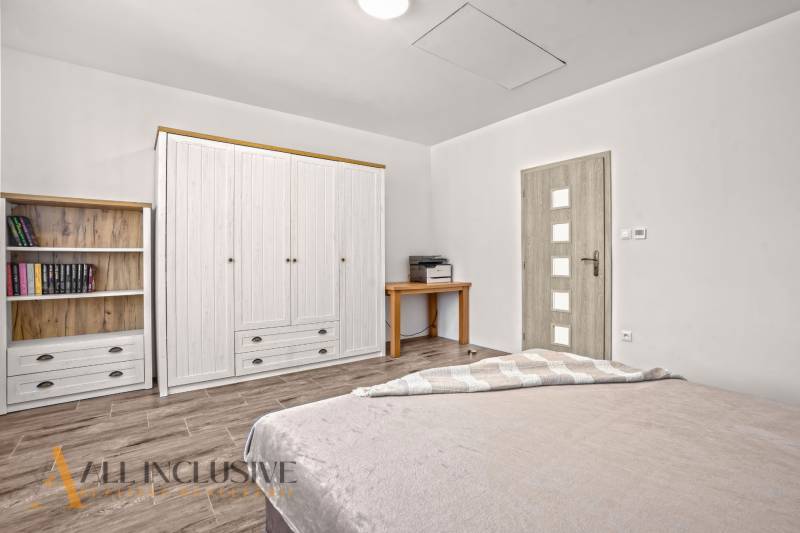 REZERVOVANÉ 3-IZBOVÝ RODINNÝ DOM V OBCI BALOŇ - Spálňa v rodinnom dome so skriňou, poličkou, stolíkom a podlahou s dreveným dekorom.