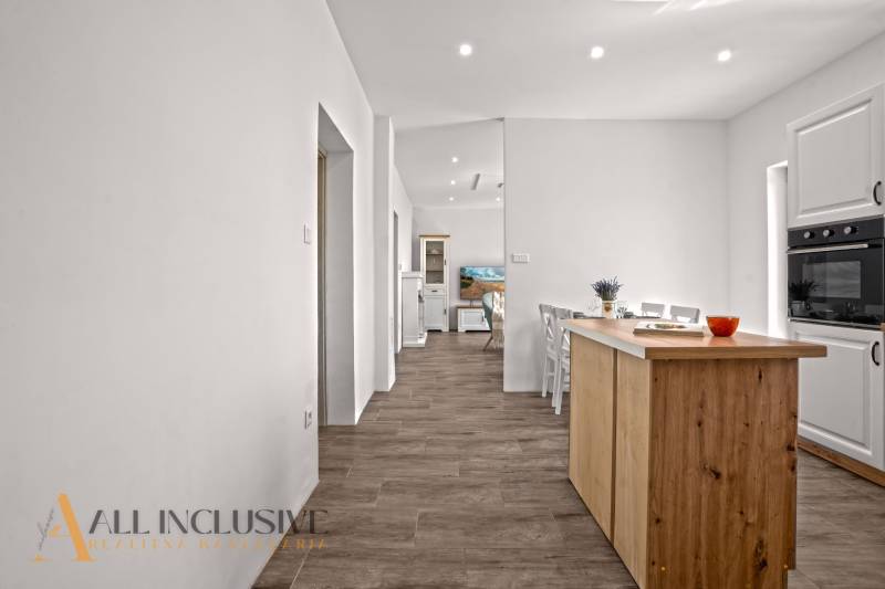 REZERVOVANÉ 3-IZBOVÝ RODINNÝ DOM V OBCI BALOŇ - Kuchyňa v rodinnom dome s podlahou s dreveným dekorom a bielym nábytkom.