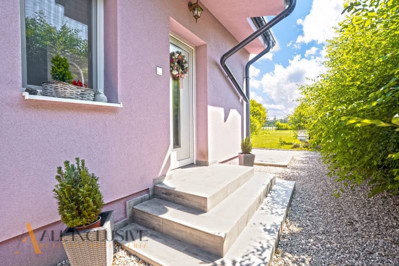 REZERVOVANÉ 3-IZBOVÝ RODINNÝ DOM V OBCI BALOŇ - Rodinný dom v Baloni s ružovou fasádou, bielymi dverami a kvetinovým dekorom.