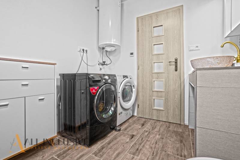 REZERVOVANÉ 3-IZBOVÝ RODINNÝ DOM V OBCI BALOŇ - Práčovňa v rodinnom dome s práčkou, sušičkou a skrinkou, podlaha s dreveným dekorom.