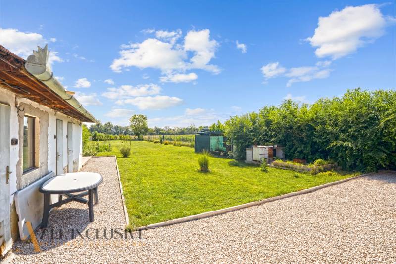 REZERVOVANÉ 3-IZBOVÝ RODINNÝ DOM V OBCI BALOŇ - Záhrada pri rodinnom dome v Baloni s trávnikom a kamenným chodníkom pod modrou oblohou.