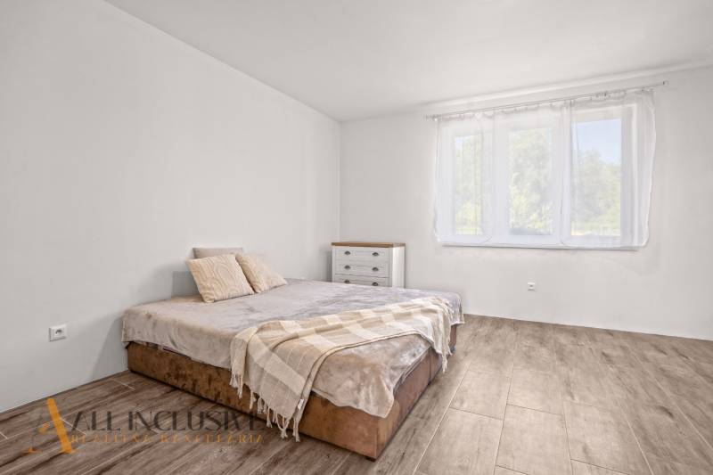 REZERVOVANÉ 3-IZBOVÝ RODINNÝ DOM V OBCI BALOŇ - Svetlá spálňa s posteľou, komodou a podlahou s dreveným dekorom v rodinnom dome.