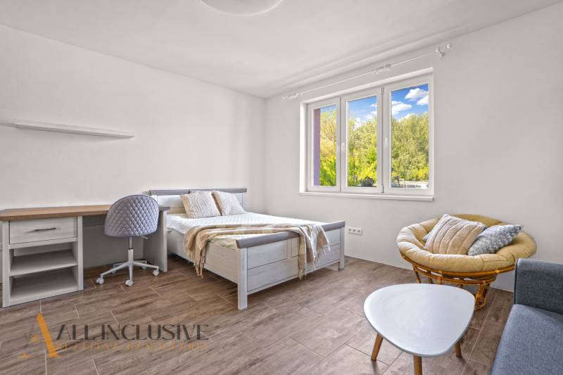 REZERVOVANÉ 3-IZBOVÝ RODINNÝ DOM V OBCI BALOŇ - Svetlá spálňa s posteľou, stolom a podlahou s dreveným dekorom v rodinnom dome.