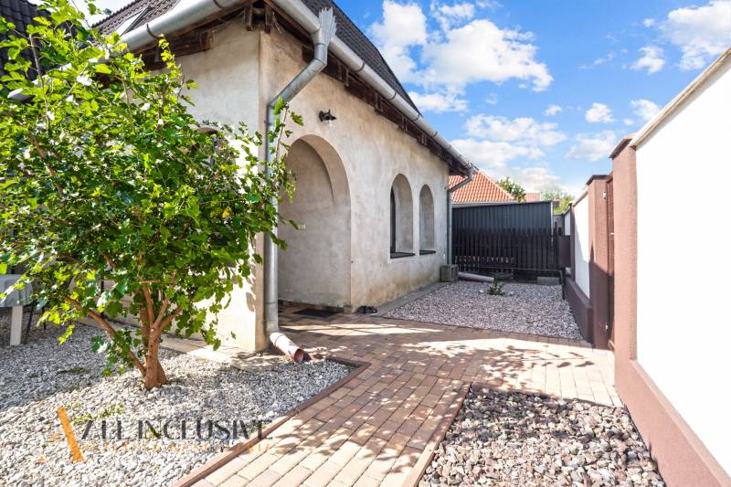 REZERVOVANÉ ZREKONŠTR. 6 IZBOVÝ RODINNÝ DOM, KOŠÚTY - Rodinný dom v Košútoch s arkádami, predzáhradkou s kamenivom a stromom, jasný deň.