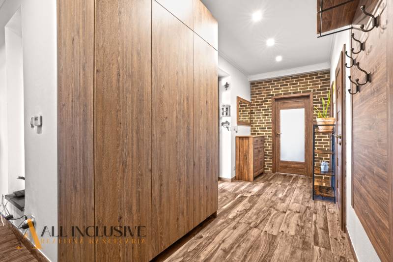 NA PREDAJ 4-IZB NOVOSTAVBA S TROJGARÁŽOU, PIN. KRAČANY - Chodba v rodinnom dome s podlahou s dreveným dekorom, skriňou a tehlovou stenou.