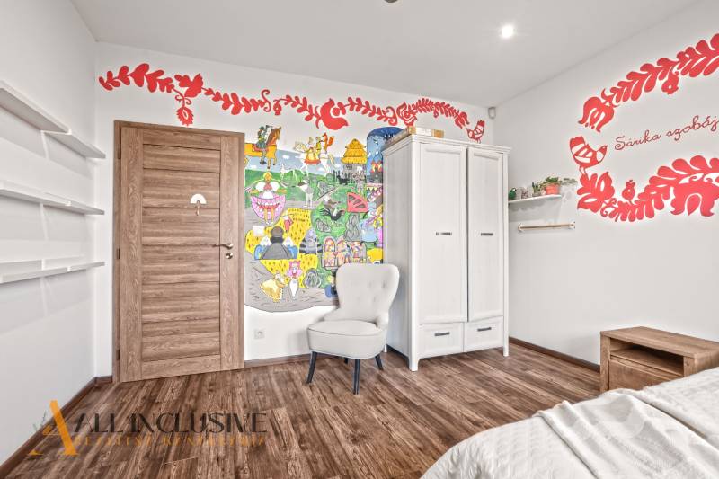 NA PREDAJ 4-IZB NOVOSTAVBA S TROJGARÁŽOU, PIN. KRAČANY - Detská izba s farebnou nástennou maľbou, skriňou a podlahou s dreveným dekorom v rodinnom dome.