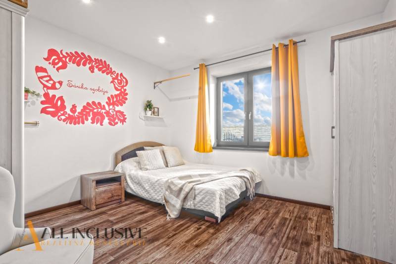 NA PREDAJ 4-IZB NOVOSTAVBA S TROJGARÁŽOU, PIN. KRAČANY - Spálňa v rodinnom dome s posteľou, nástennou dekoráciou a podlahou s dreveným dekorom.