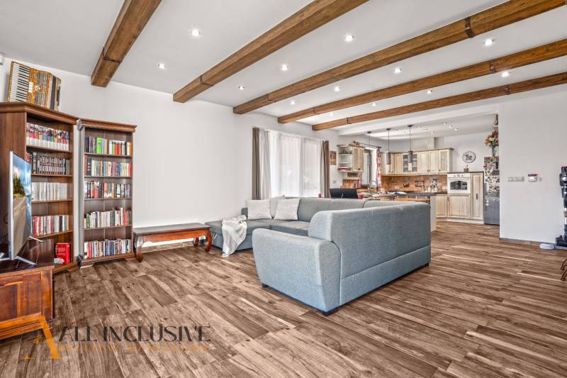 NA PREDAJ 4-IZB NOVOSTAVBA S TROJGARÁŽOU, PIN. KRAČANY - Obývacia izba v rodinnom dome s podlahou s dreveným dekorom, pohodlnou sedačkou a knižnicou.