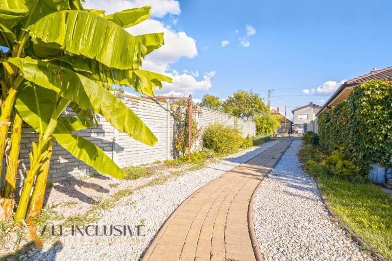 NA PREDAJ 4-IZB NOVOSTAVBA S TROJGARÁŽOU, PIN. KRAČANY - Rodinný dom v Pinkových Kračanoch, Dunajská Streda s dláždeným chodníkom obklopeným zeleňou a banánovníkom.